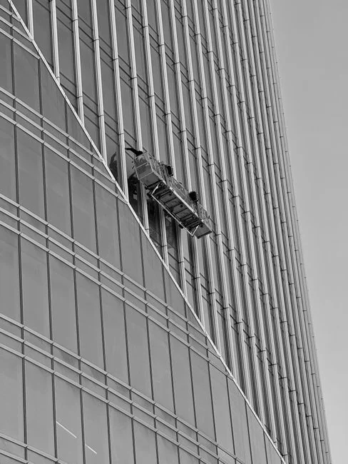 Two workers hanging to clean windows on a modern skyscraper facade.