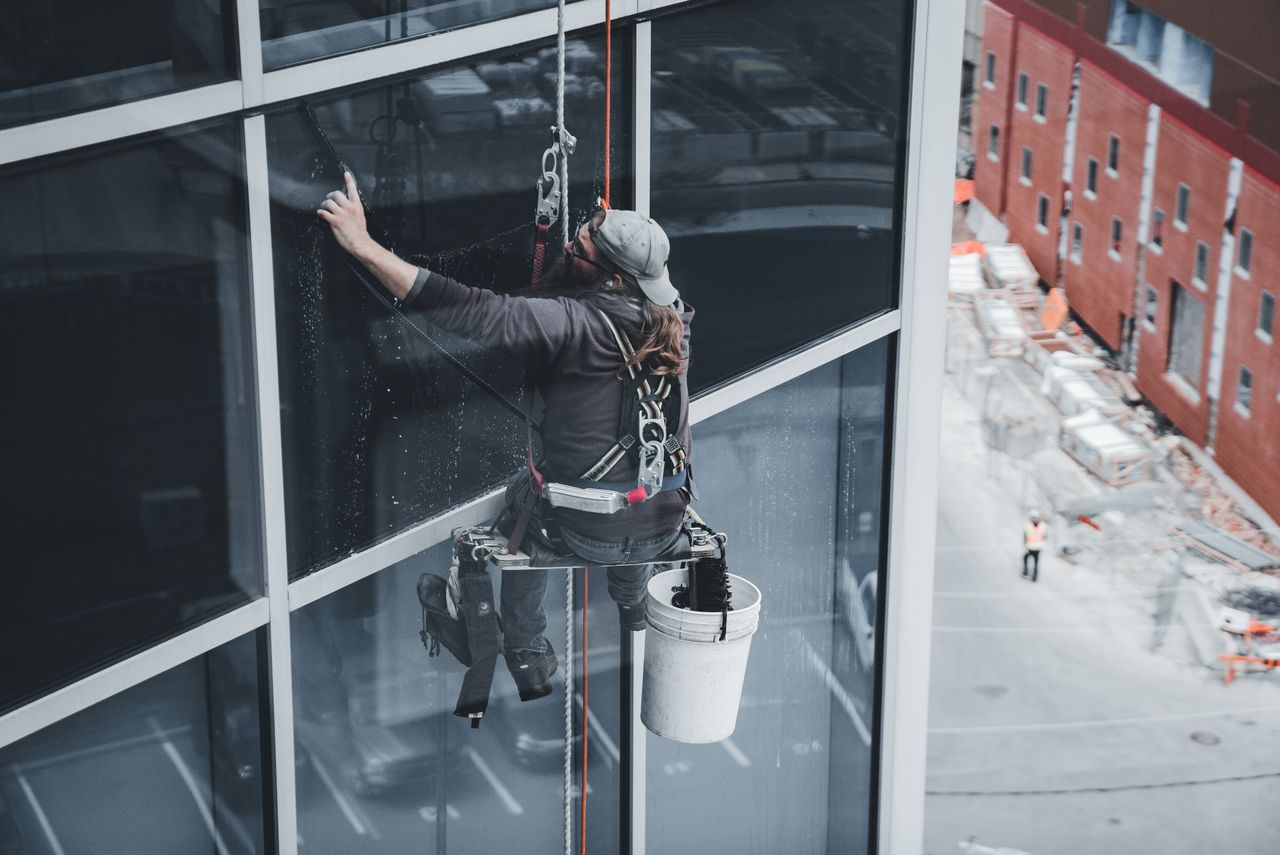 hero-img A worker washing windows on a skyscraper while wearing a harness in an urban environment.